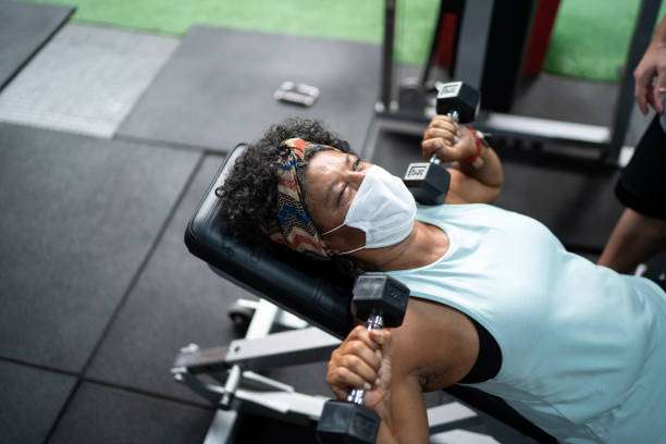Idosa com máscara facial fazendo exercícios numa academia