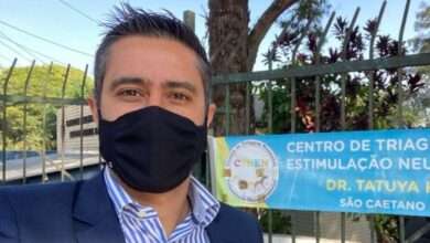 Caio Salgado usando máscara preta e camisa listrada em frente ao CTNEN - Centro de Triagem Neonatal e Estimulação Neurossensorial
